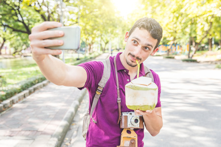 Man take a selfie and drink coconut water in Bangkok. Tourist with vintage camera and backpack...