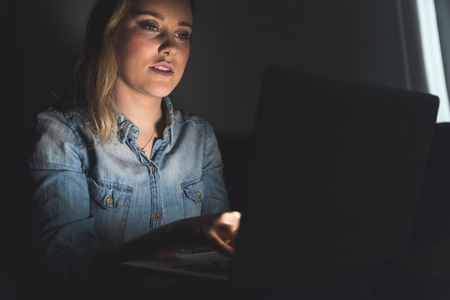 Woman with computer on her lap working at home. Beautiful girl typing on keyboard and looking at the...