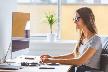 Young woman at work, talking on the phone and looking at computer. Home office or small company...
