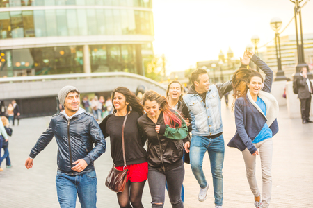 Multiracial group friends having fun in the city at sunset - Happy people in London, boys and girls walking and jumping together - Playful and happy mood, lifestyle situation about friendshipの写真素材