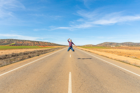 Happy successful man jumping in countryside road - Young man wearing checked shirt triumph a victory with a jump and raising arm - Happiness and success concepts, taken in Spainの写真素材