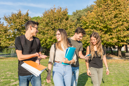 Happy students at park carrying books and having fun - Small group of teenage best friends together at park after school - Sunny summer day in Italyの写真素材