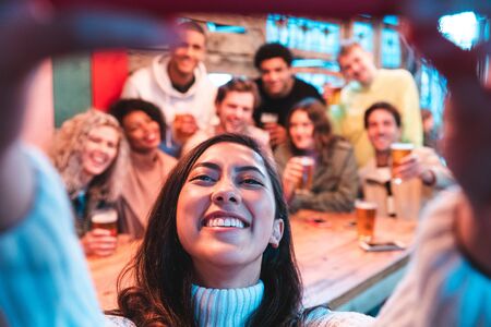 Happy friends taking a group selfie at pub - Group of multiracial millennial people having fun together at pub and taking a photo - Birthday party or after work meeting, happiness and teamwork conceptsの写真素材