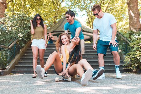 Group of friends having fun with skateboard at park. Multi ethnic people enjoying time together and...