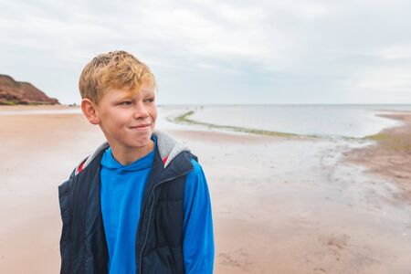 Boy alone portrait on the beach on cloudy day - Kid with blond hair alone at seaside looking away from cameraの写真素材