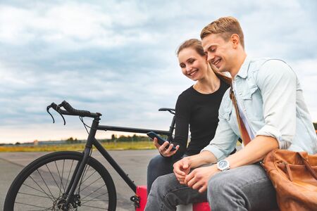 Happy couple together using smartphone and smiling - Man and woman sharing time together, sitting next to a fixed gear bike and looking at the phone - friendship and lifestyle conceptsの写真素材