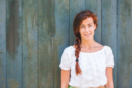 Smiling girl with braid portrait on green wooden background - redhead young woman looking at camera - empty space to add text on the leftの写真素材
