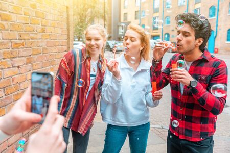 Happy friends playing with soap bubbles together - Multiracial group of teenagers best friends enjoying time together in London - Lifestyle and friendship in Londonの写真素材