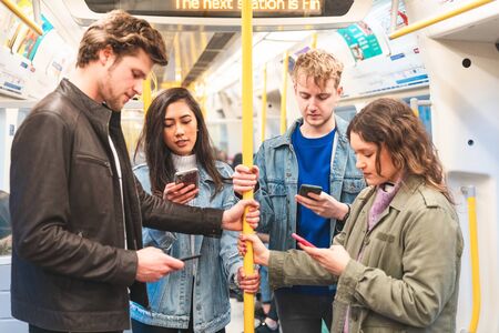 Busy tube, people looking at smartphones and texting - Multiracial group of friends together in subway metro train in London - Travel, lifestyle and commuting in millennials lifeの写真素材