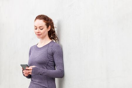 Woman using mobile phone after training session - beautiful young woman wearing gym fitness clothes checking outdoor activity statistics - healthy lifestyle, sport and technology conceptsの写真素材