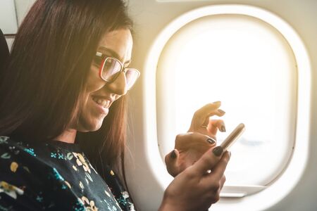 Woman travelling by airplane typing on her smartphone - Beautiful and smiling happy young woman texting with her mobile phone while on a trip - travel and technology conceptsの写真素材