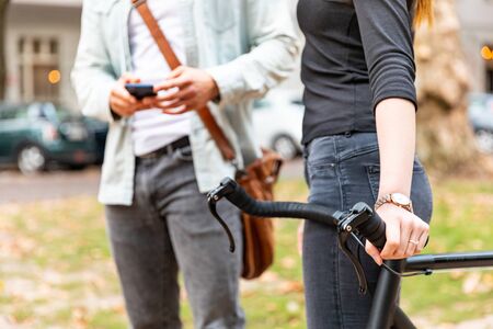 Close up of woman with a bike and man with phone together in a city park - couple commuting and walking together in Berlin in a sustainable way - friendship and lifestyle conceptsの写真素材