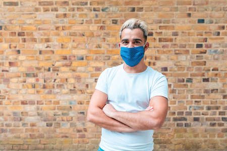 Young man portrait with face mask on - Man wearing a white t-shirt posing in front of a brick wall in London - lifestyle and happiness during coronavirurs pandemicの写真素材