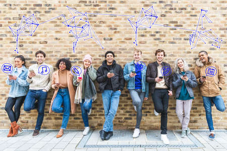 Millennial group of friends using smartphones, icons popping out from screens and links above - Group of young adult with phones and glowing icons of email, music, calendar, phone etc - Technology and lifestyle conceptsの写真素材