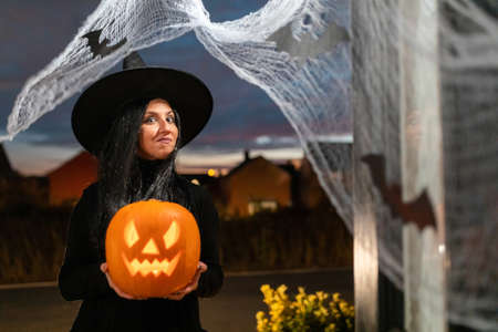 Woman witch carrying a pumpkin for Halloween night - Spooky scene with halloween symbols and signs  - holidays, culture and lifestyle in UK and United Statesの写真素材
