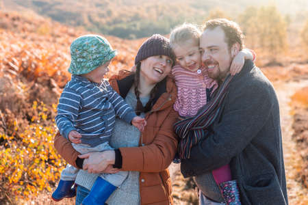 Happy family portrait embracing together on a sunny autumn day - Mother and father holding their daughter and son and having fun all together in a cute group hugの写真素材