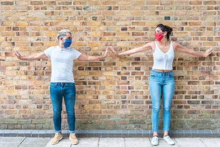 Couple with face mask keeping social distance - Young man and woman outdoors during coronavirus pandemic using arms to keep apart from each otherの写真素材