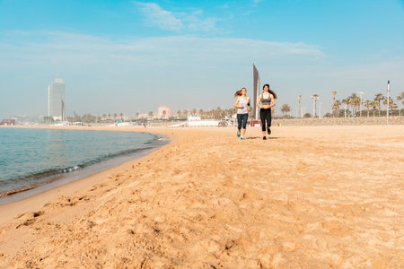 Two women jogging on the beach in Barcelona - beautiful and sportive young women working out in the early morning at seaside - Sport and healthy lifestyleの写真素材