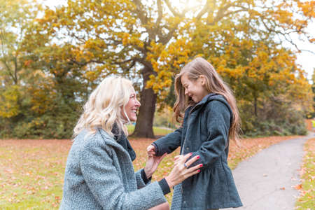 Mother and daughter at park in autumn in London - Happy mom and girl wearing warm clothes on a funny day out together - fall season lifestyle imageの写真素材