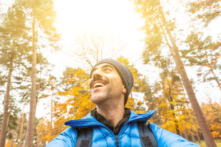 Happy man taking a selfie in the wood with beautiful autumn vibes - Young man alone enjoying time in a remote forest away from city and busy life - lifestyle and natureの写真素材
