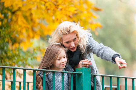 Mother and daughter at park in autumn in London - Happy mom and girl wearing warm clothes on a funny day out together - fall season lifestyle imageの写真素材