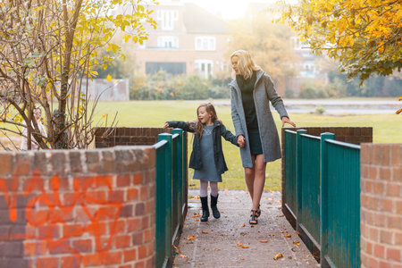 Mother and daughter at park in autumn in London - Happy mom and girl wearing warm clothes on a funny day out together - fall season lifestyle imageの写真素材