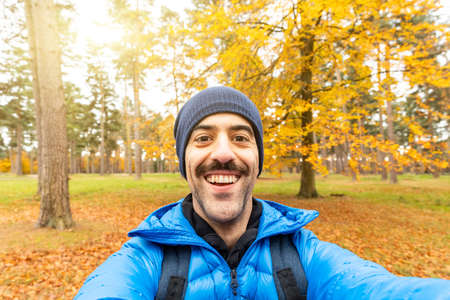 Happy man taking a selfie in the wood with beautiful autumn vibes - Young man alone enjoying time in...