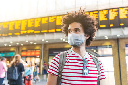 Man portrait wearing face mask at train station in London - Mixed race young man with curly hair waiting for train on an essential journey during coronavirus lockdownの写真素材