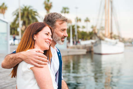 Happy adult couple relaxing on the pier in Barcelona - Man and woman together on a summer sunny day in Barcelona, hugging and looking at boats - Love and lifestyle conceptsの写真素材