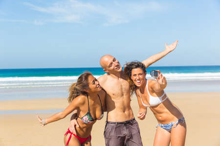 Happy multiracial friends taking a selfie at seaside - Multiethnic people having fun together in sunny Fuerteventura - Man and women at beach enjoying time togetherの写真素材