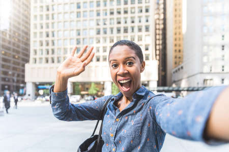 Happy woman waving to the camera and laughing - Black woman with short hair taking a selfie or videocall in Chicago - Lifestyle and technology conceptsの写真素材