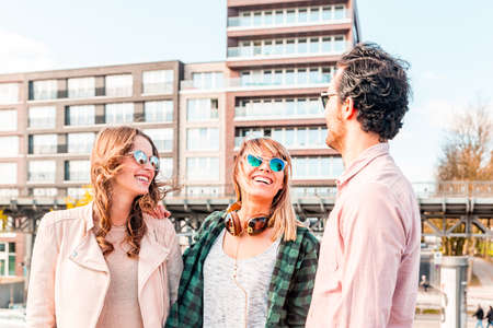 Happy multiracial group of friends having fun together in Hamburg - Two women and one man, smiling and talking with a blue sky on background - Friendship and lifestyle conceptsの写真素材
