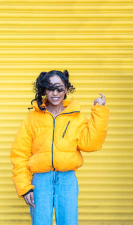 Happy black woman portrait with yellow background playing with hair and smiling - Beautiful mixed race young woman wearing yellow top and curly hair - happiness and lifestyle conceptsの写真素材