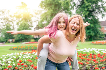 Woman and girl playing at park and enjoying piggyback ride - Mother and daughter having fun together...