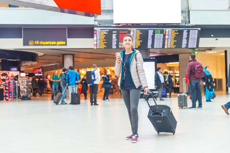 Happy woman at the airport waiting in the departure hall - Young woman with carry-on luggage waiting to go to the gate - Lifestyle and travel conceptsの写真素材