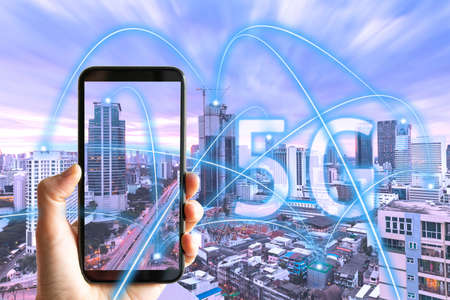 5G smart city communication network concept - Hand holding smartphone with Bangkok skyline on background with abstract links connecting buildings, wireless, visualisation of the internet of thingsの写真素材