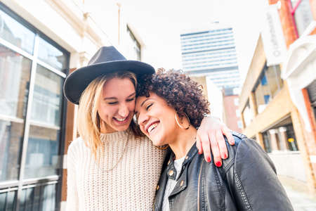 Authentic happy lesbian mixed race couple enjoying time out in the city on a sunny day - Two women embracing and laughing together, lifestyle and gay conceptsの写真素材