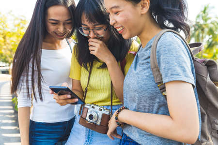 Three happy asian girls using phone and looking at screen together having fun and laughing while...