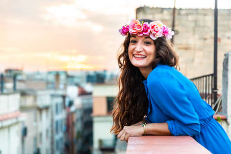 Happy smiling woman portrait on a rooftop in Barcelona. Young caucasian woman wearing a flower crown hair band and looking at camera. Happiness and joy, copy space on the leftの写真素材