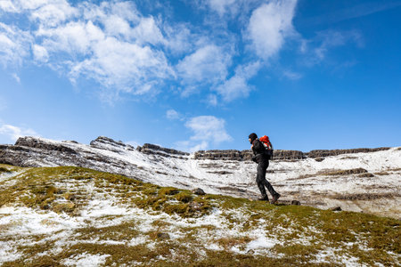Man hiking in Scotland, Isle of Skye, with snowy mountains on background - Hiker climbing up a ridge on a winter day - Travel and adventure conceptsの写真素材