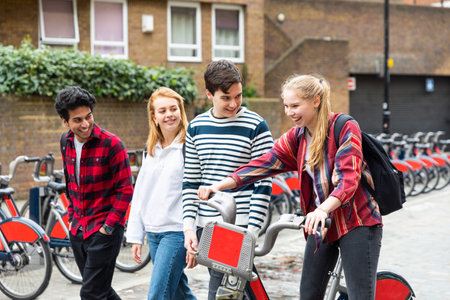 Teen group of friends walking in the city and pushing a bike - Multiracial group of teenagers best friends enjoying time together in London - Lifestyle and friendship in Londonの写真素材