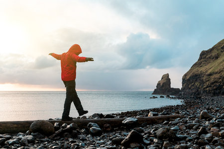 Man hanging in the balance over a log at seaside in Scotland - Hiker having fun at beautiful destination Talisker bay after the rain - Filter applied, travel and adventure conceptsの写真素材