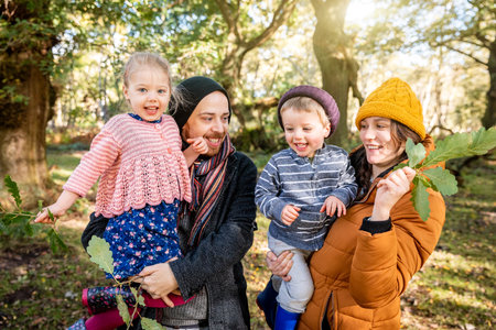 Happy family portrait together in the wood - Mother and father holding their daughter and son and having fun all together on a sunny autumn day in the nature - Family and lifestyle conceptsの写真素材