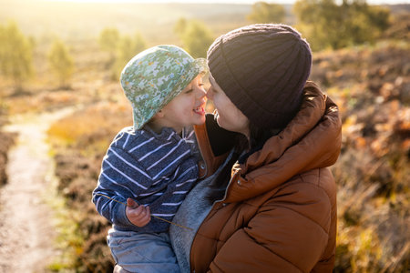 Cute family portrait with mother and son playing and cuddling - Happy authentic moment on a sunny autumn day outdoorsの写真素材