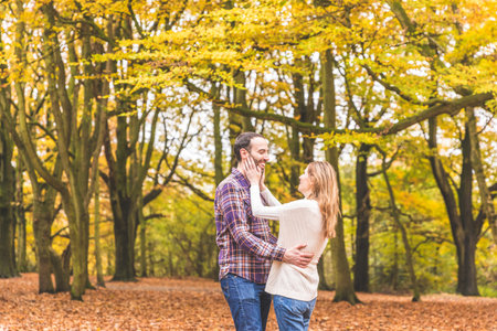 Authentic adult couple enjoying a day out in the wood in autumn with trees on background - Happy man and woman cuddling and smiling, love and lifestyle conceptsの写真素材