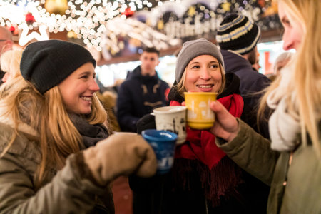 Happy young women with cups of mulled wine at Christmas market in Innsbruck - Smiling girls enjoying hot drink to keep warm on a cold night in Austria - Lifestyle and culture conceptsの写真素材