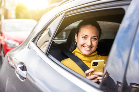 Happy woman portrait sitting on the back seat of a taxi car in the city looking out of the window - Smiling young caucasian woman using phone and car service - Travel and commuting conceptsの写真素材