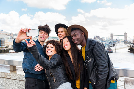 Group of friends taking a selfie together in London - Multiracial mixed race friends on a trip getting a picture with Tower Bridge on background - Travel and lifestyleの写真素材