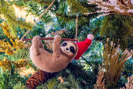 Closeup of a stuffed sloth wearing a Santa Claus hat ornament hanging from a Christmas treeの写真素材