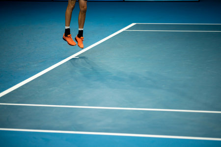 Tennis player serving in a tennis match, with leg drive in a game of sport  in the evening under lightsの写真素材